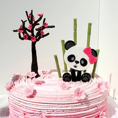 Torta cubierta con crema rosada, con un panda y un árbol en flor de azúcar encima